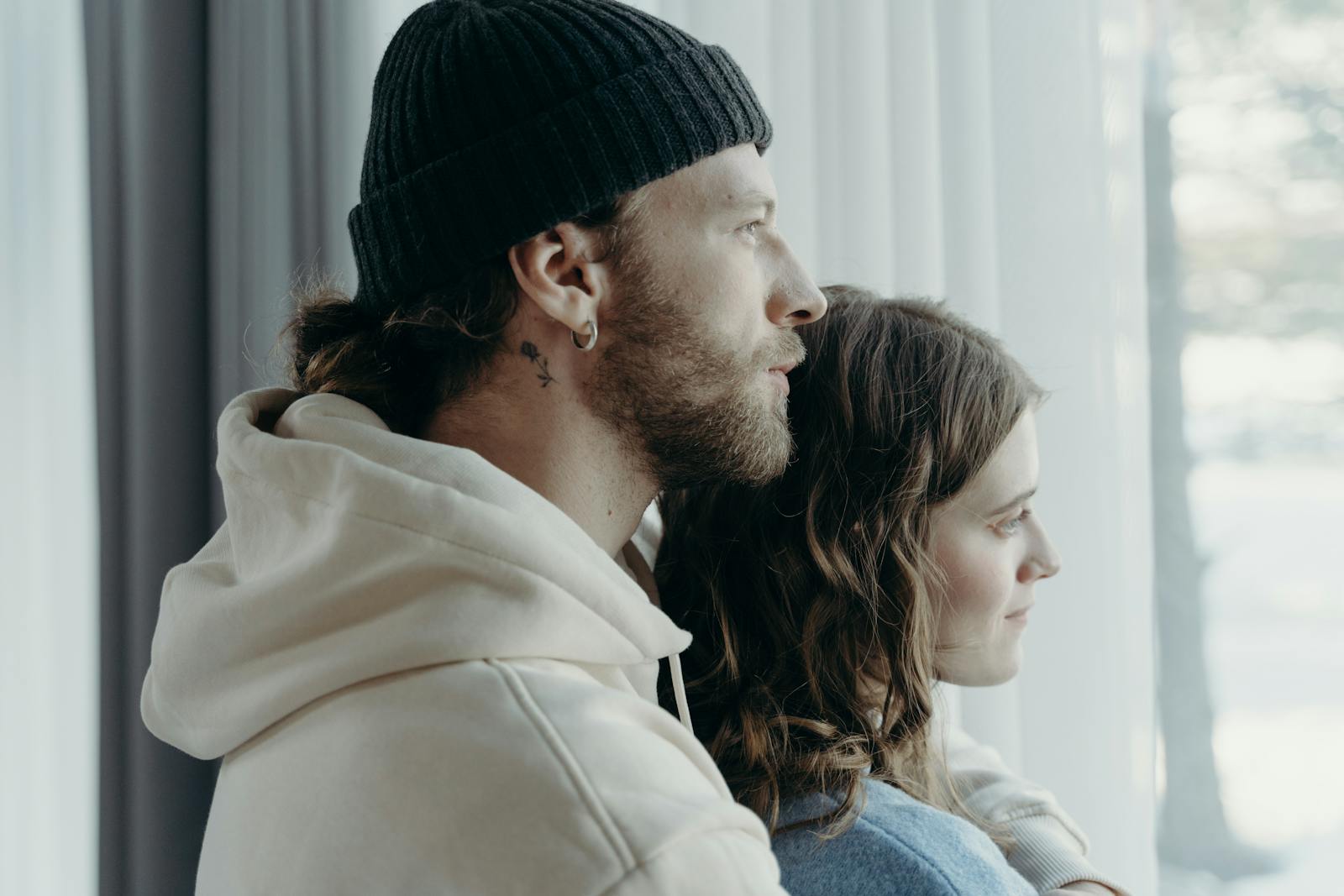 Intimate portrait of a couple embracing while looking outside a window, capturing warmth and affection.