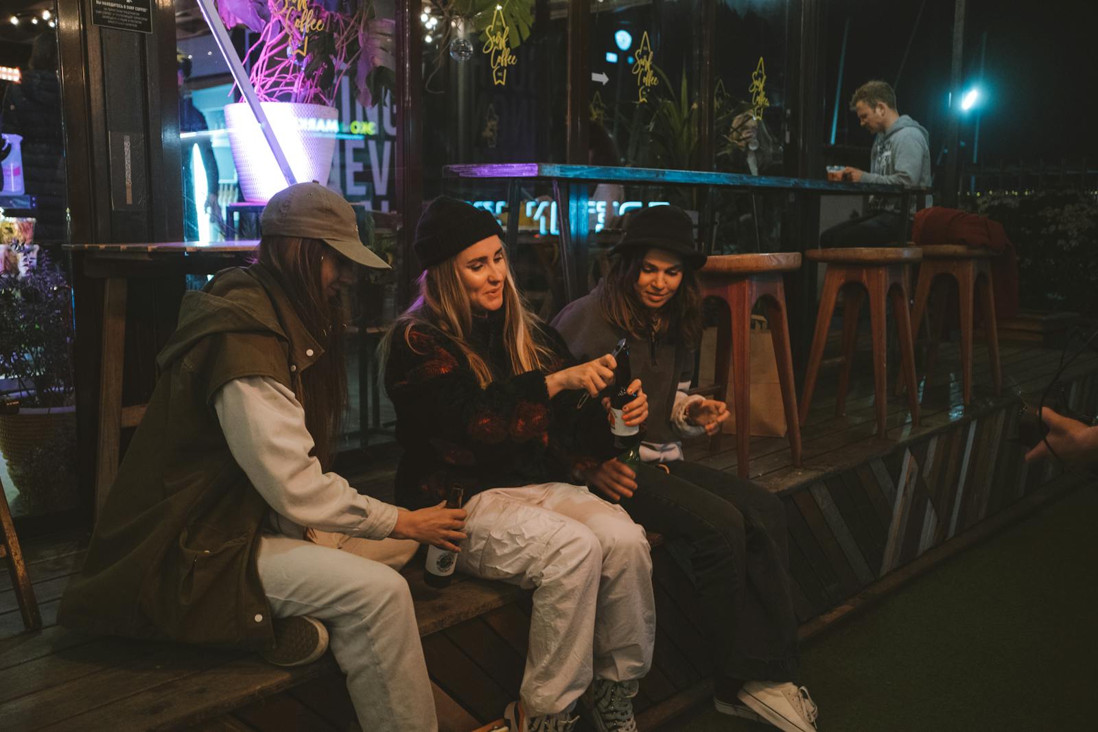 Three young women enjoy drinks and friendship at an outdoor bar during the evening.