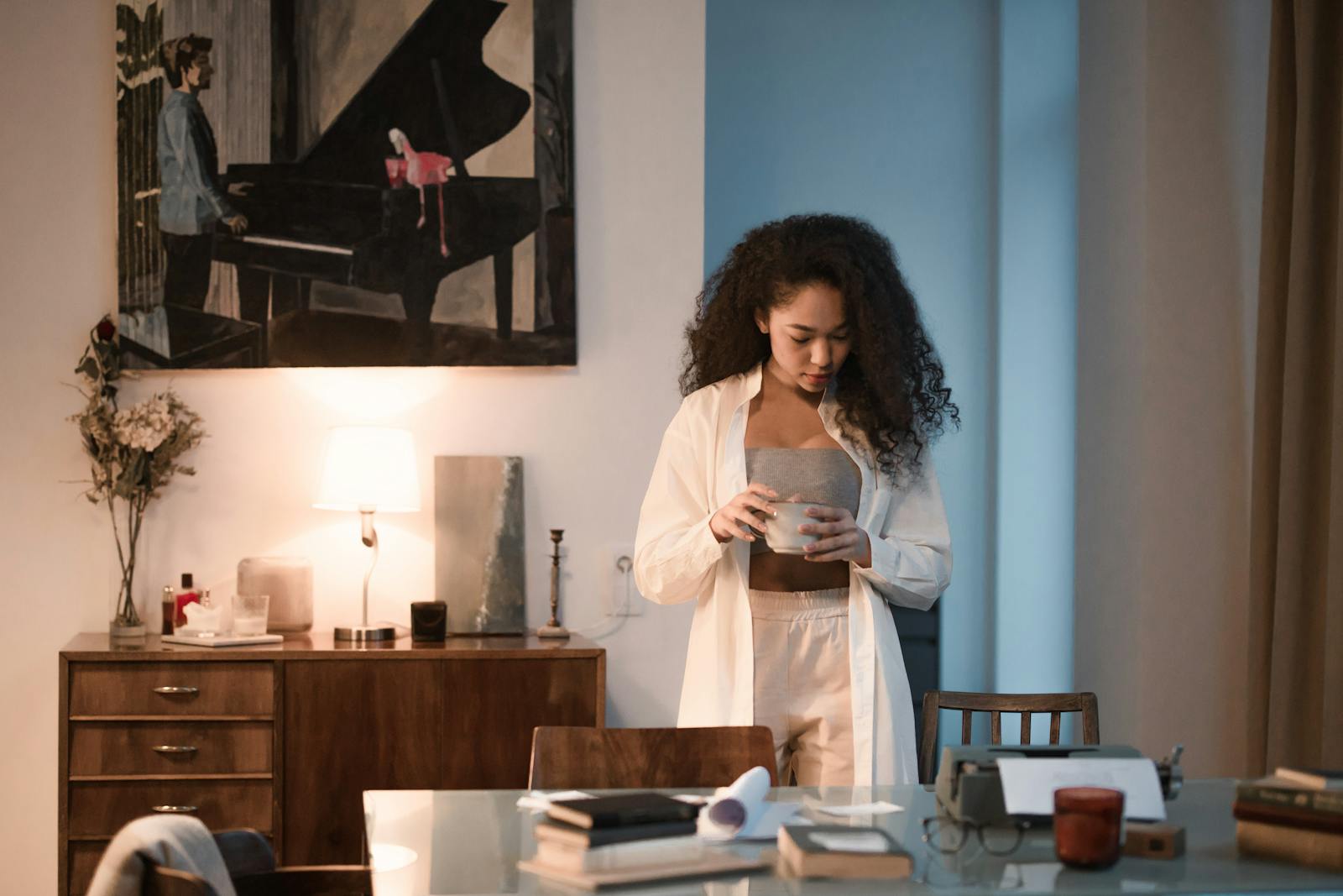 Young woman enjoying coffee in a cozy home office setting with warm lighting.