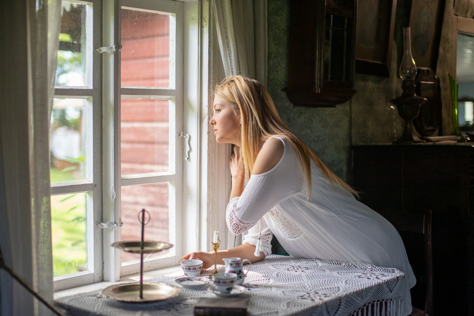 Young woman in white dress looking out a window.