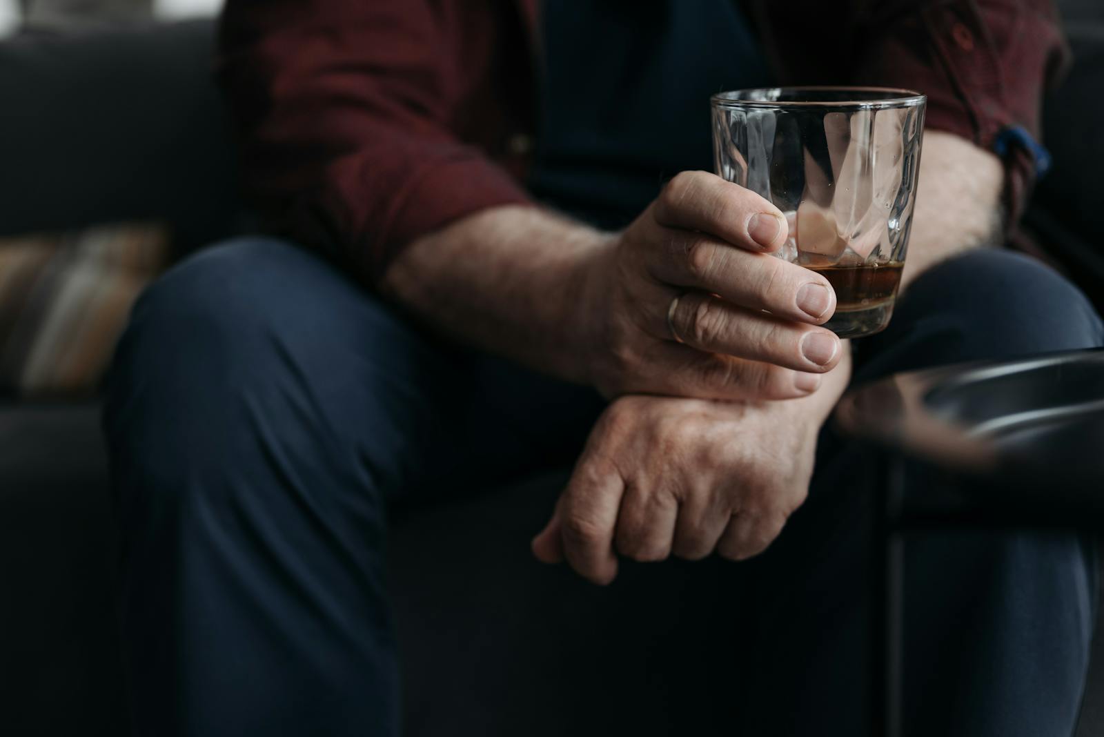 A detailed image of an adult hand holding a whiskey glass indoors.