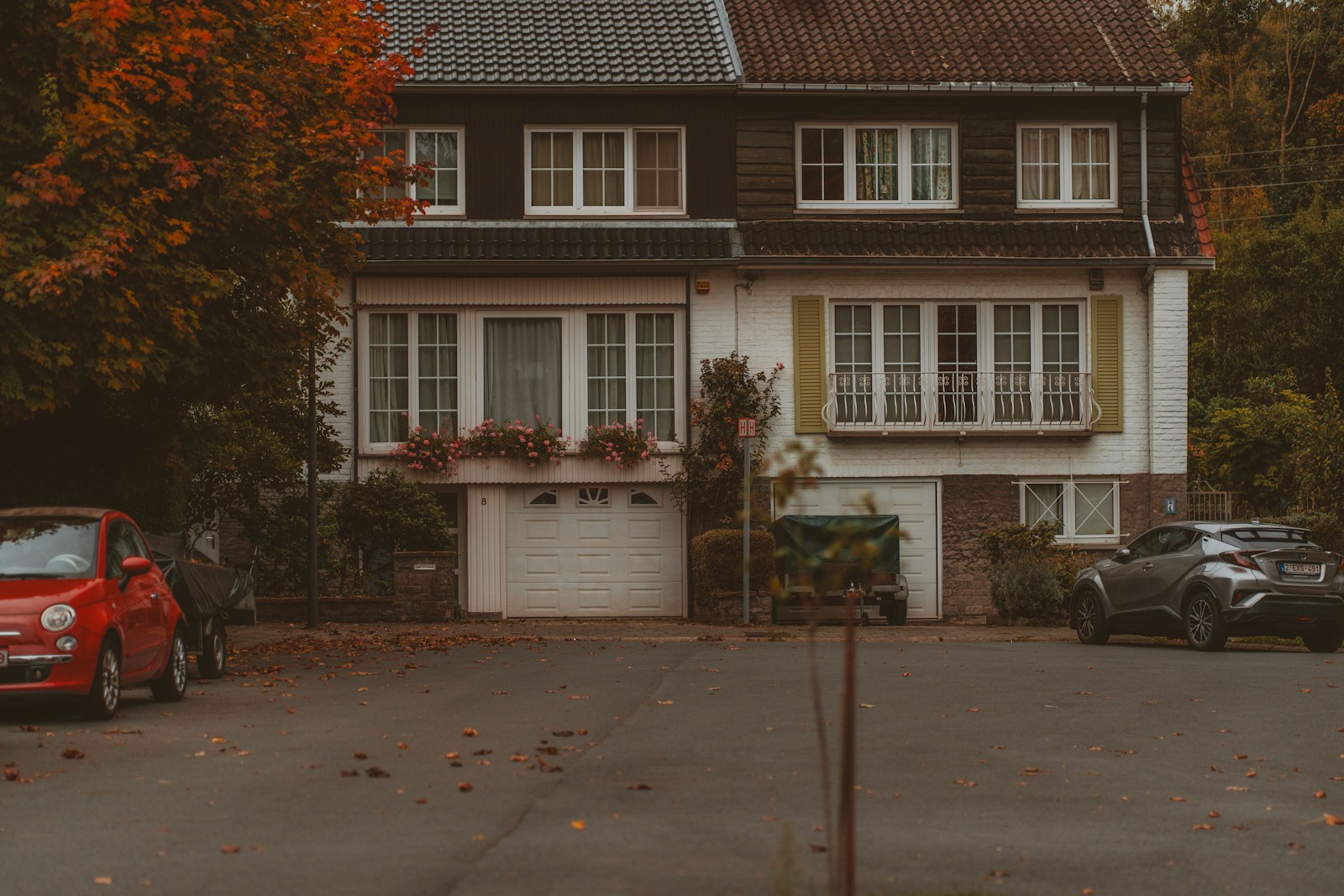 Two cars parked outside a suburban house in autumn.