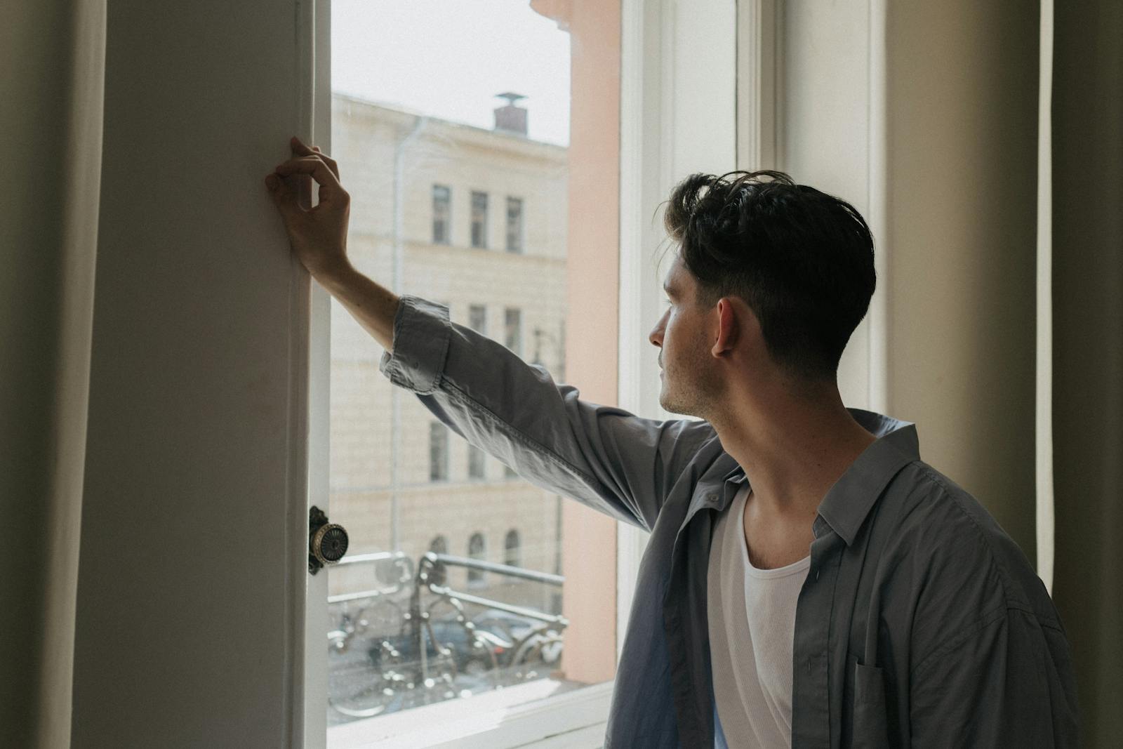 A man gazes thoughtfully out a window in a well-lit room, capturing a moment of introspection.