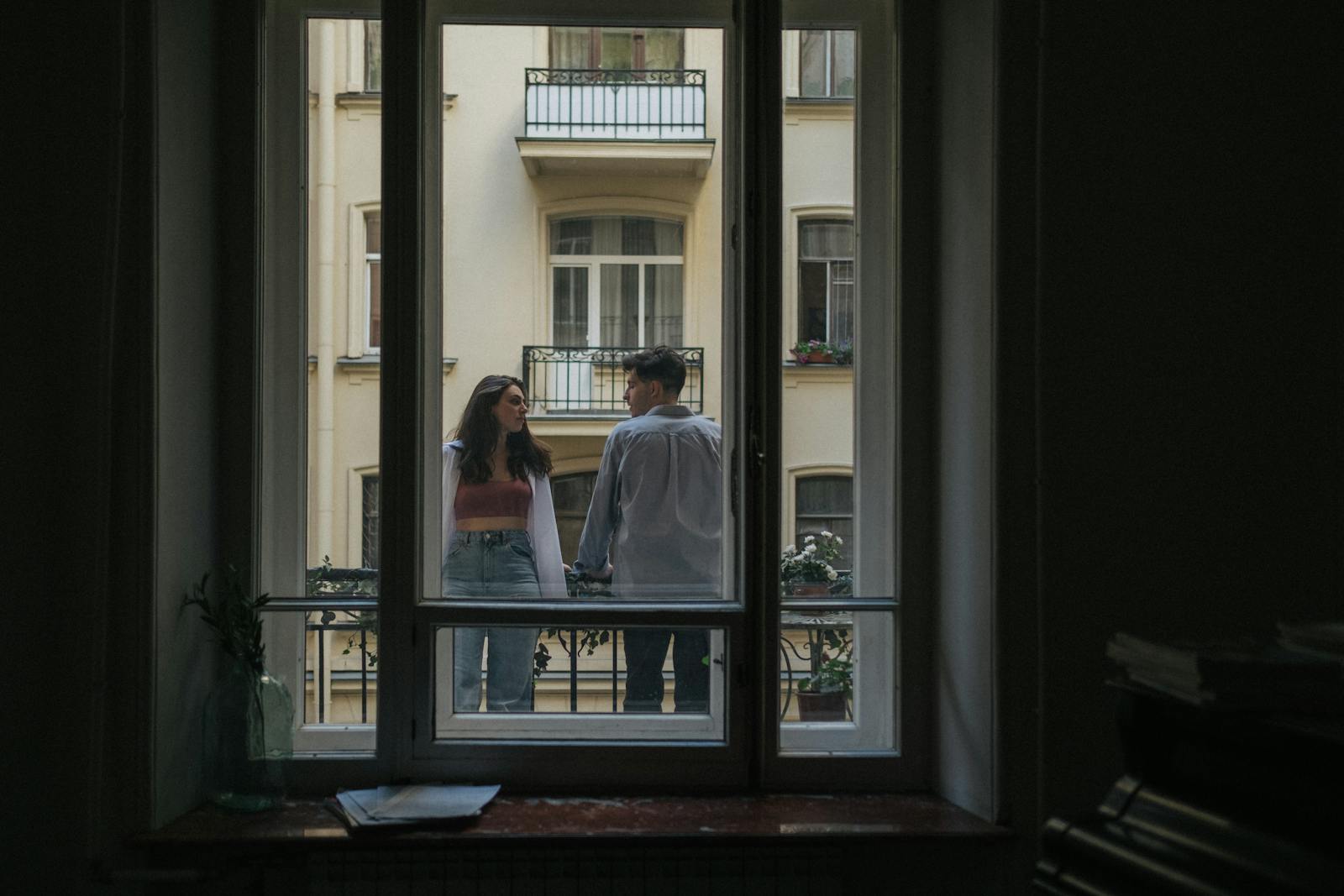 Couple enjoying a moment together on a balcony, framed by a window.