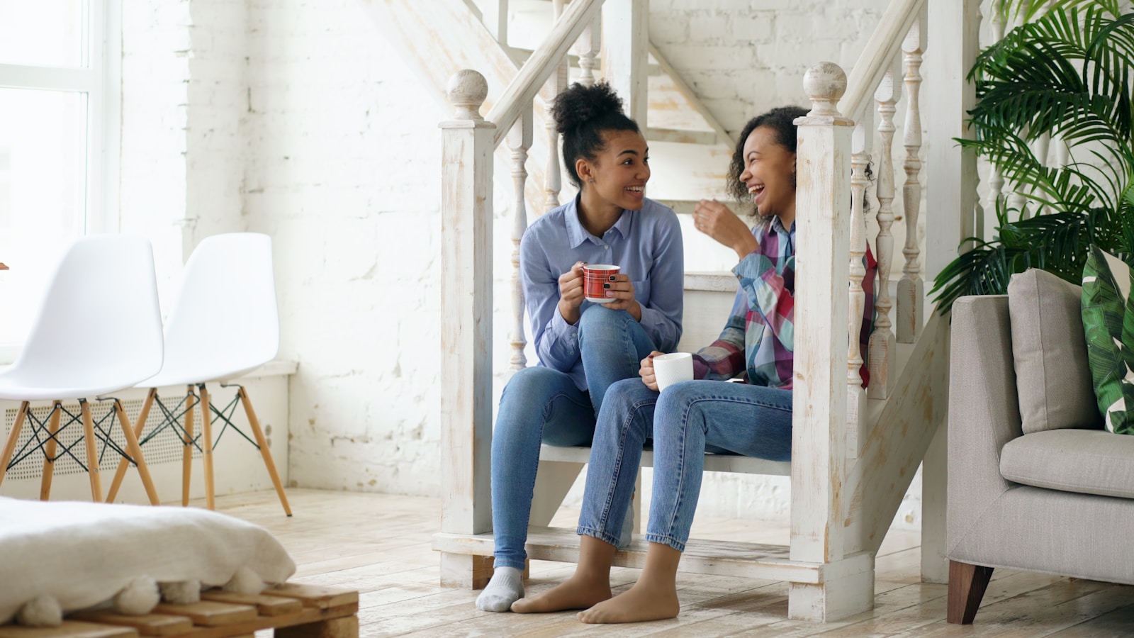 Two women talking and drinking coffee on stairs.