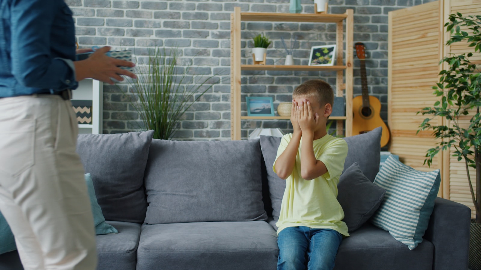 Child hides face while adult stands nearby.