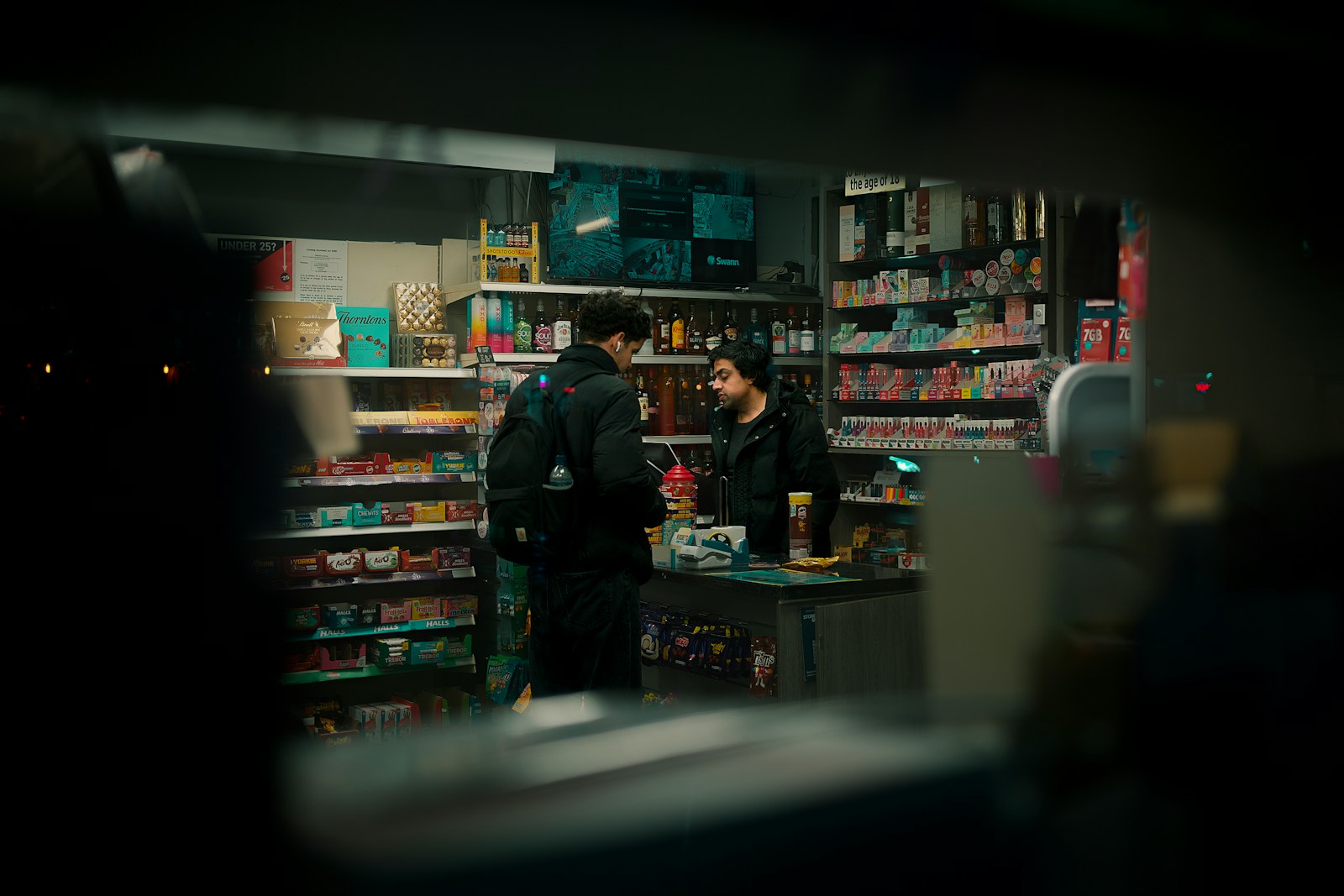 Two men talking inside a brightly lit convenience store.