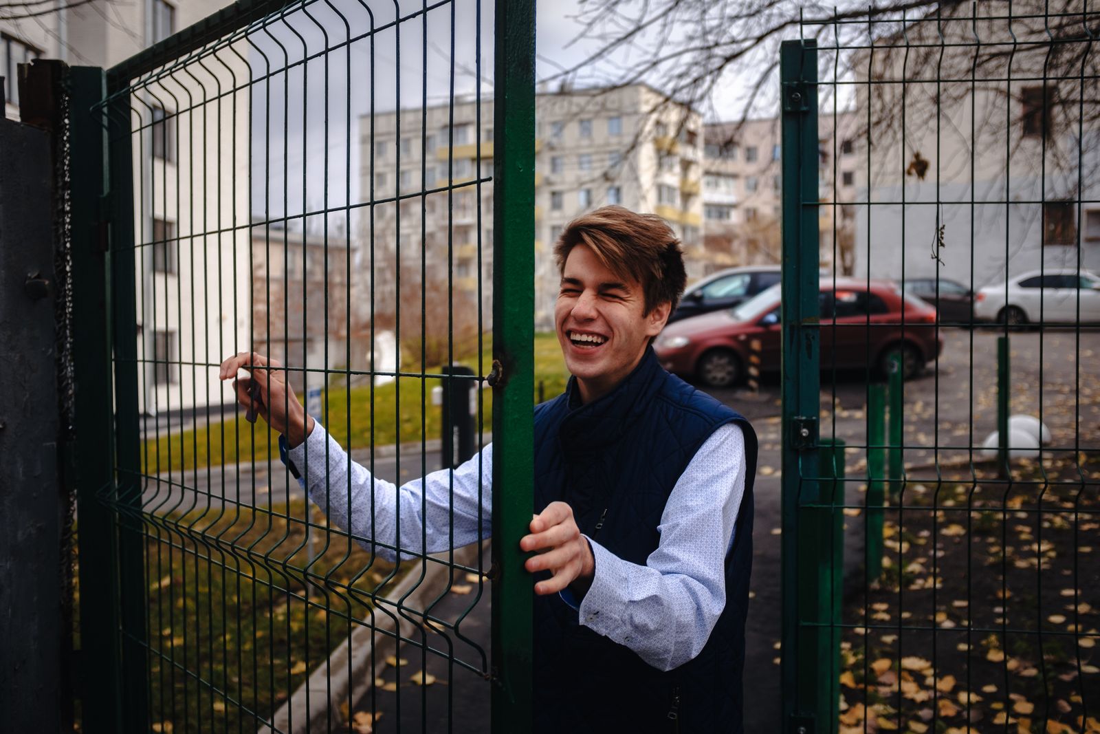 Happy young man in a blue vest entering through an open metal gate on a fall day in the city.