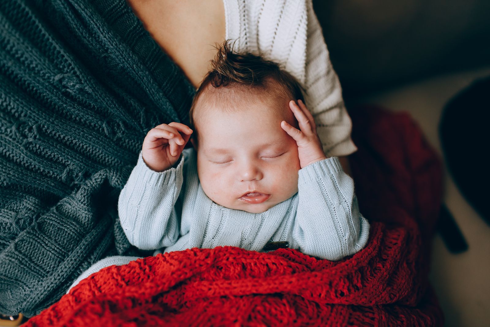 A peaceful newborn baby sleeps comfortably in warm, colorful blankets.
