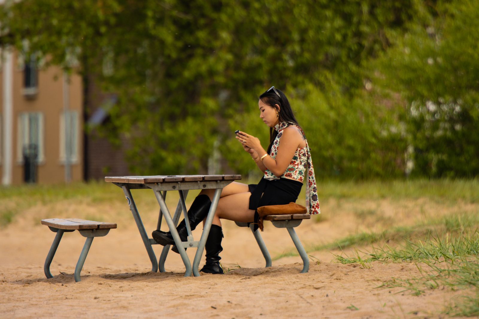 Young woman using smartphone at picnic table in a sunny outdoor setting in Sweden.