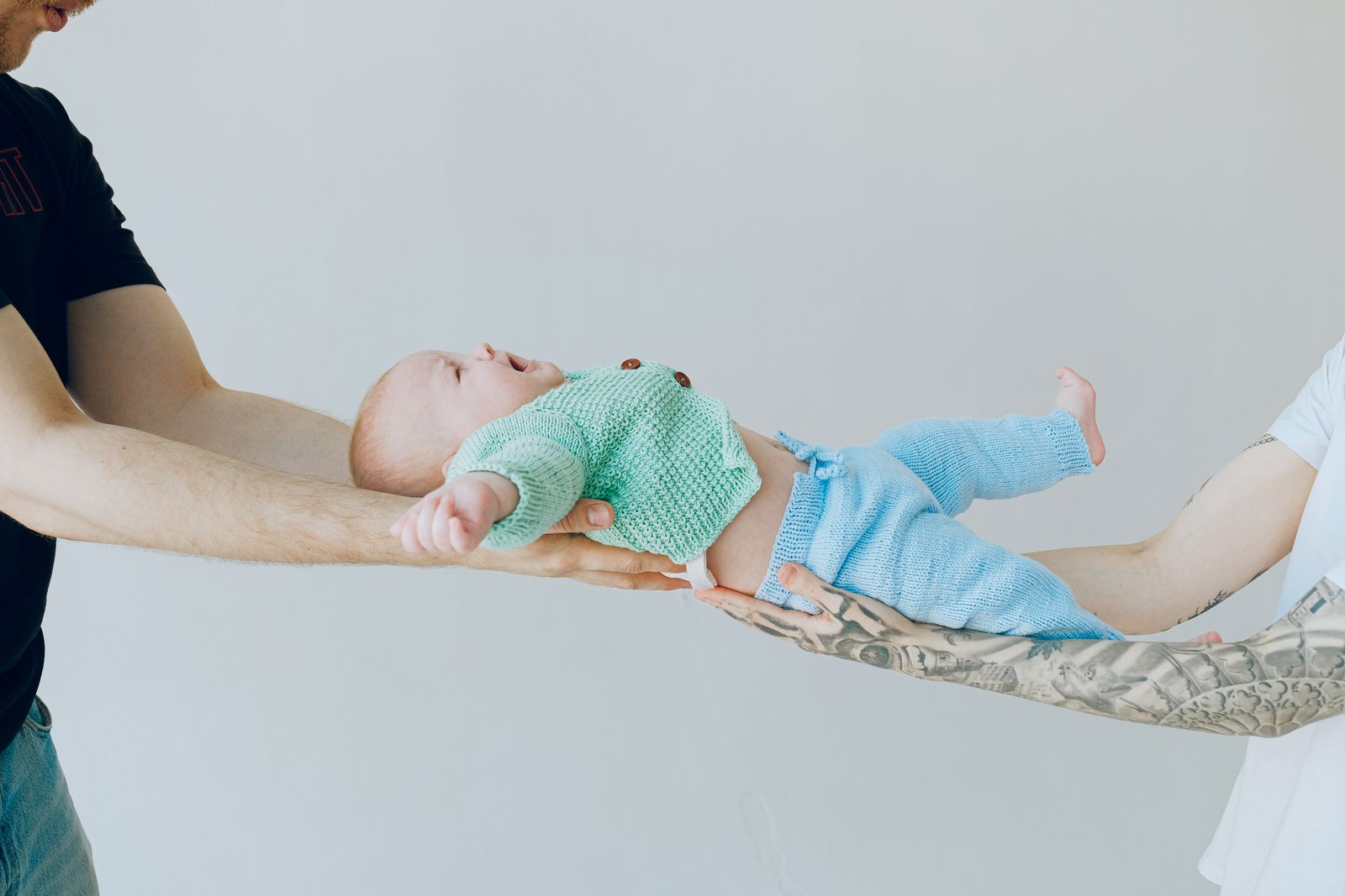 Two parents lovingly lift their newborn baby in knitwear, symbolizing family bond and happiness.