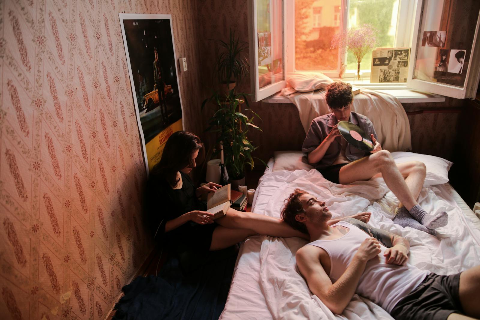 Three friends relaxing in a cozy bedroom, reading and listening to vinyl records.