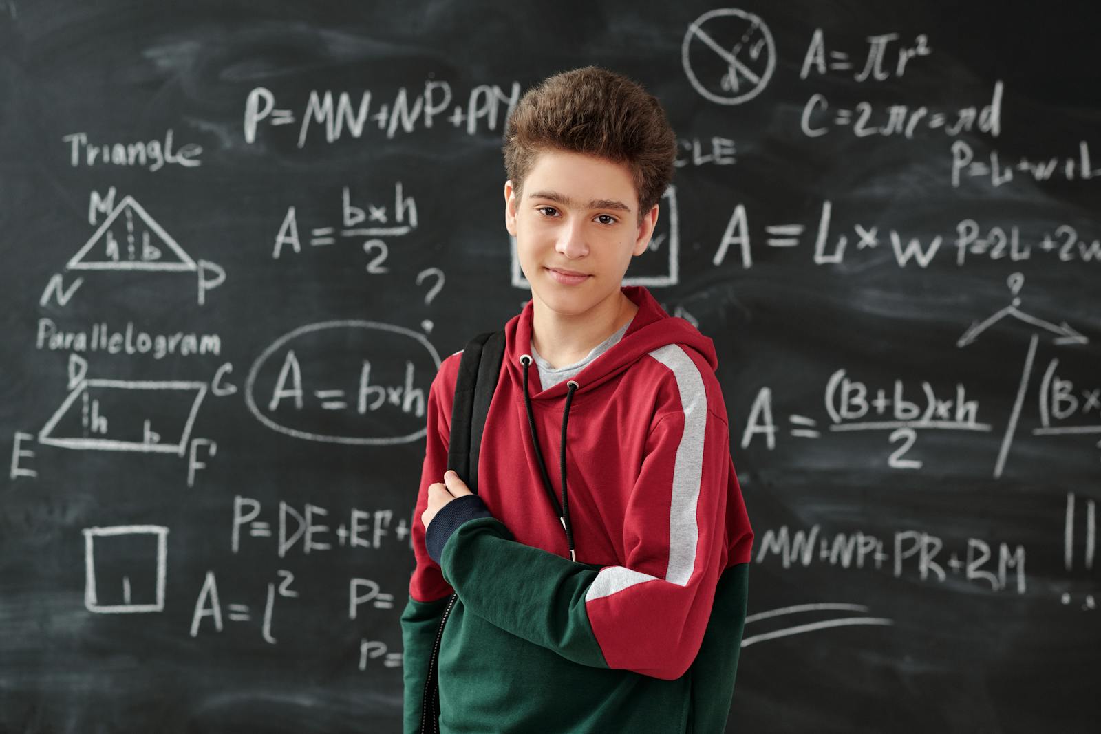 Teenage boy standing confidently in front of a blackboard filled with math formulas, showcasing his passion for learning.