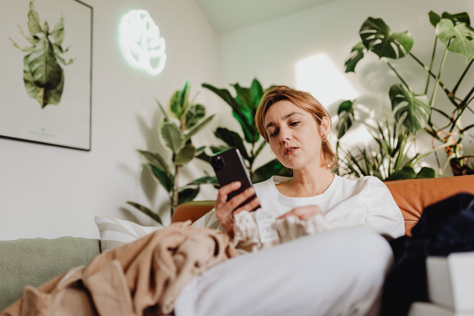 Comfortable living room scene with woman using smartphone among houseplants.