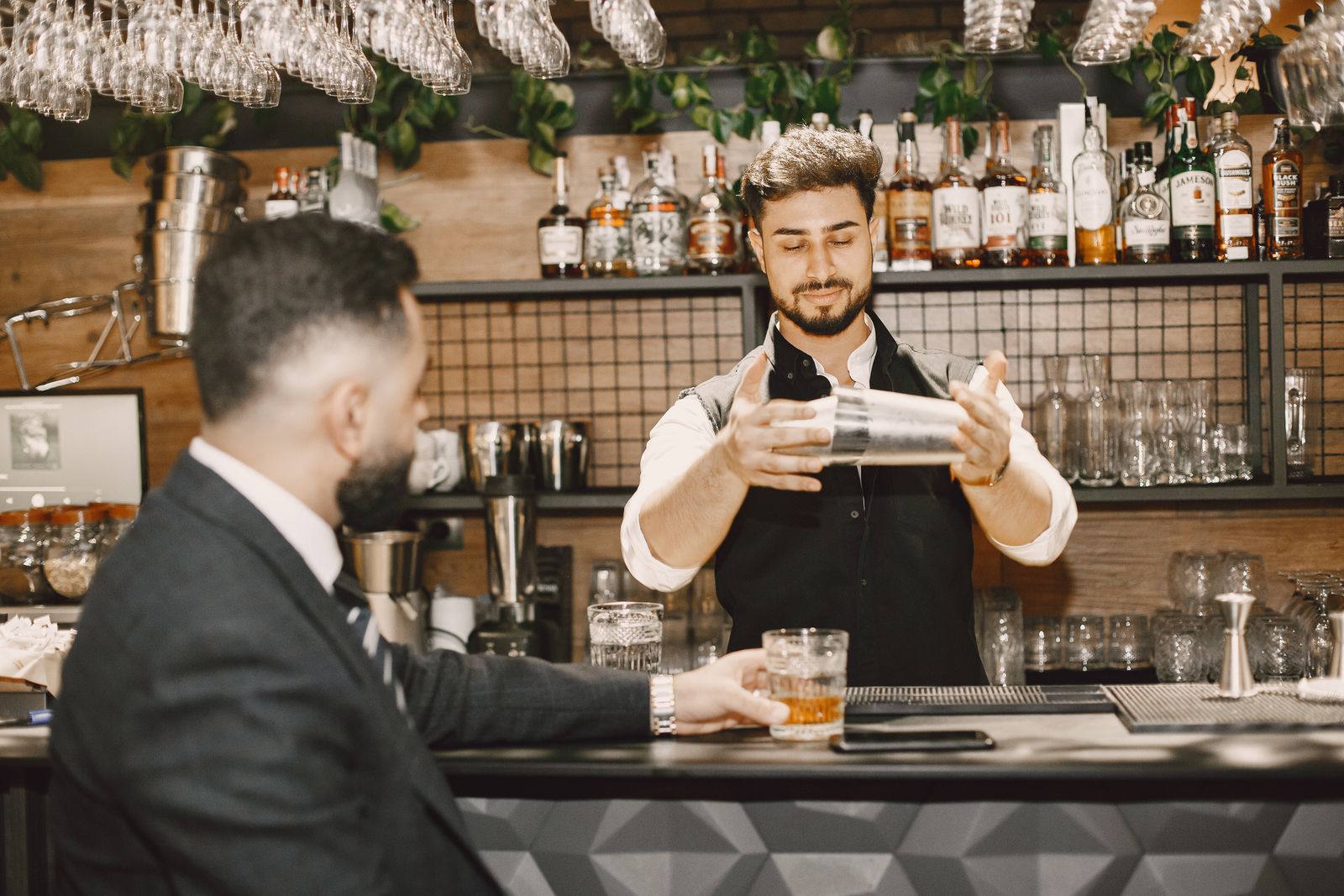 Bartender expertly mixing a drink in a stylish bar with patrons.