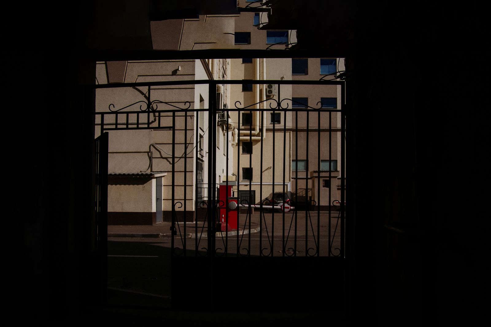 A view through a decorative metal gate displaying an urban courtyard.