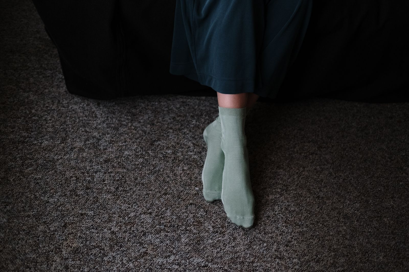 From above of crop anonymous female in socks sitting with crossed legs on carpet in house