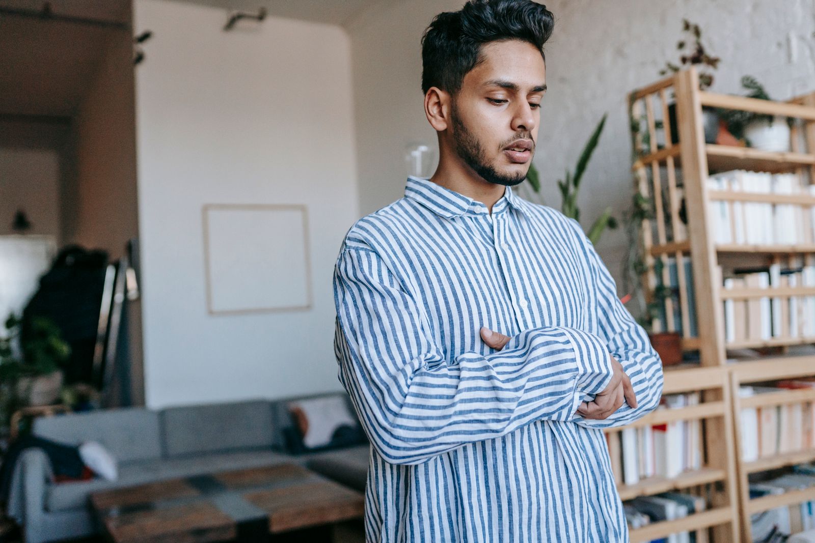 A young man in a striped shirt stands in prayer inside a modern home, embodying peace and reflection.