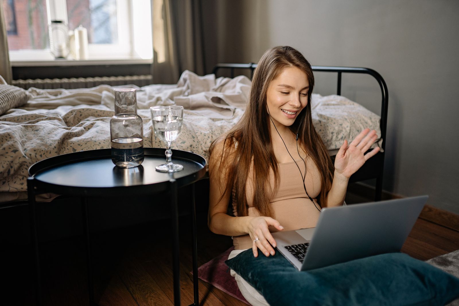Smiling woman works remotely on laptop while sitting on the floor. A cozy indoor setting ideal for digital nomads.