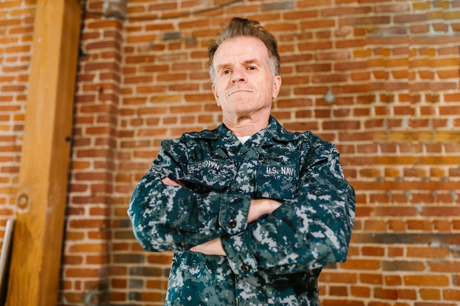 Proud US Navy veteran standing confidently in military uniform with brick background.