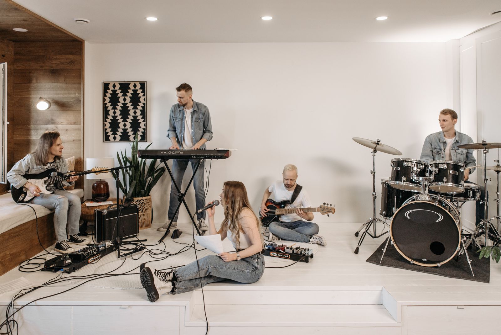 A group of friends performing music with various instruments in a modern home setting.