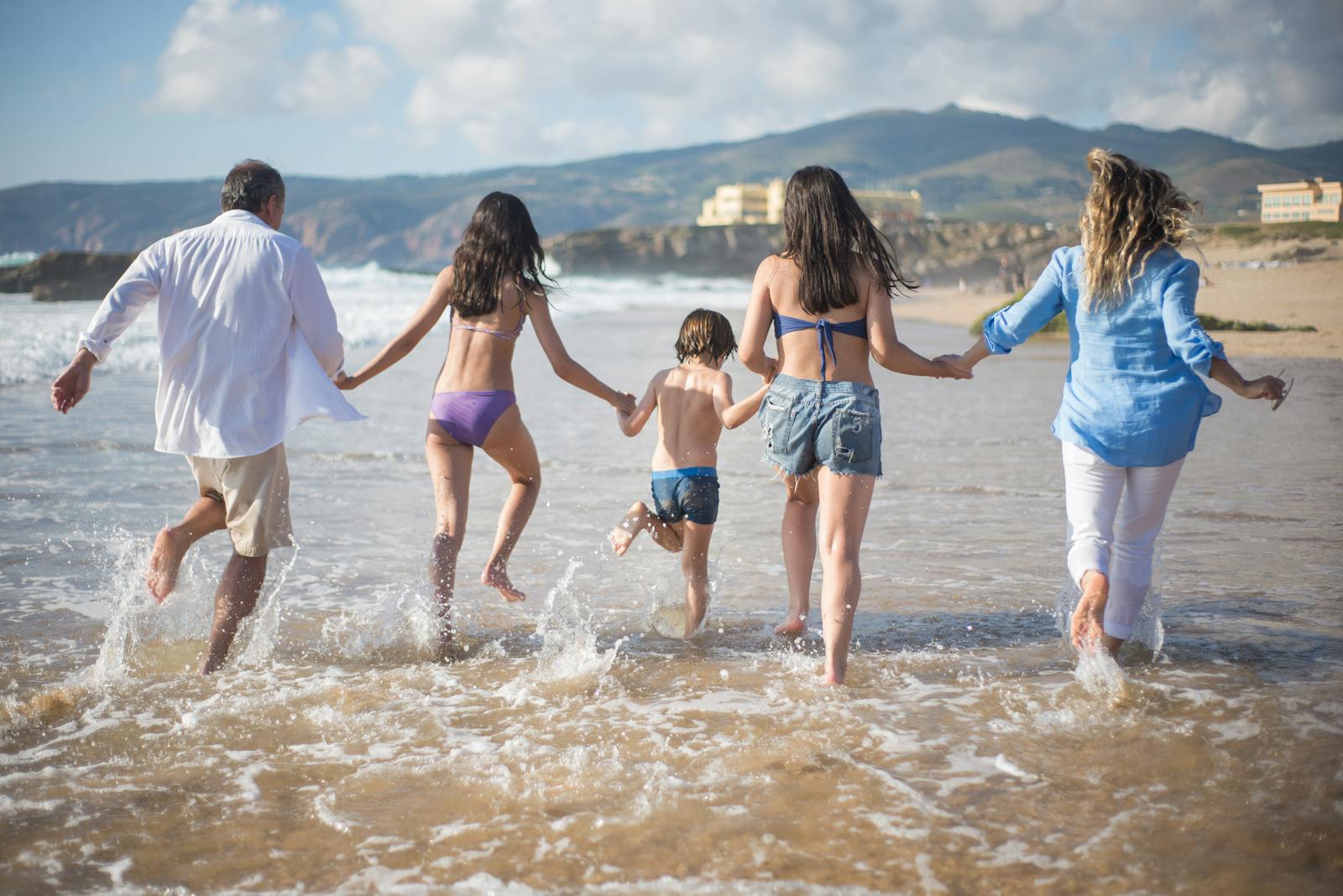 A family having fun running into the ocean on a sunny beach day in Portugal. Joyful and carefree moments.