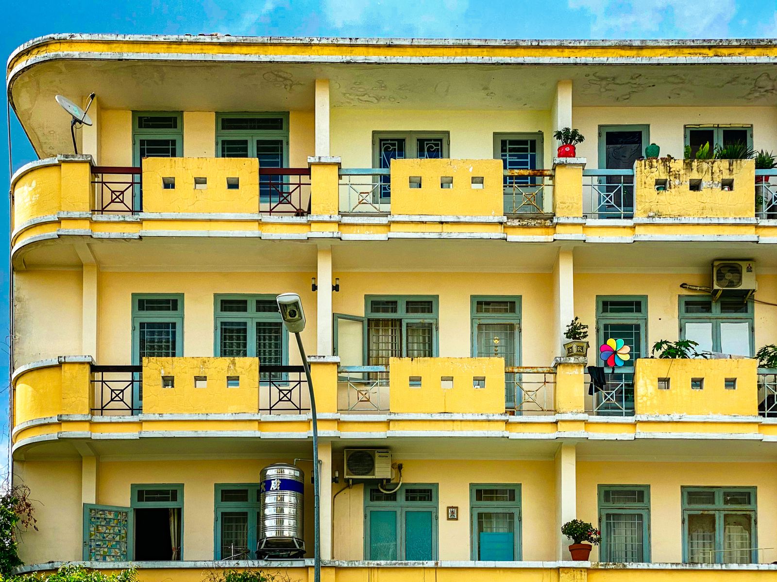 Colorful residential building with yellow balconies, windows, and potted plants.