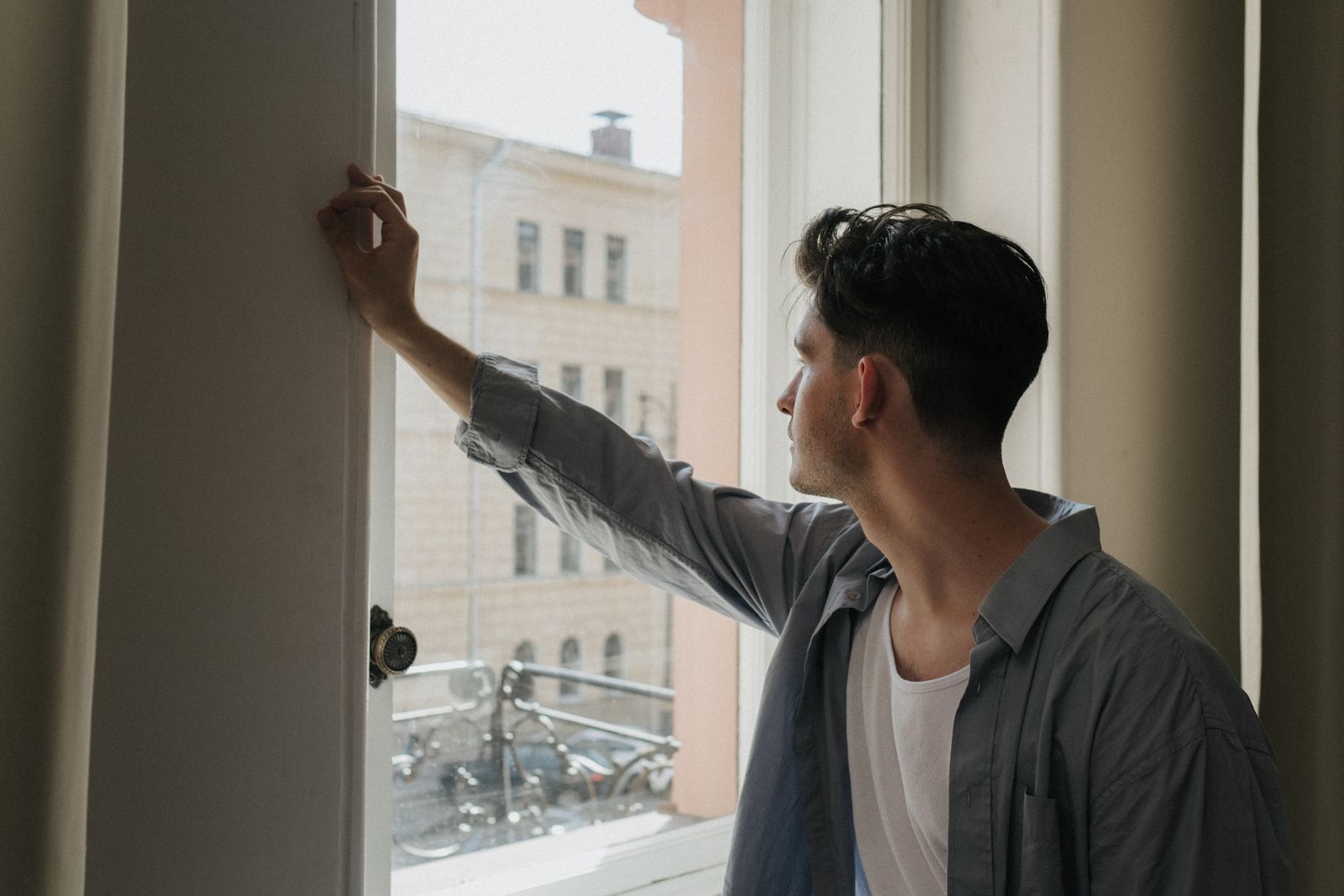 A man gazes thoughtfully out a window in a well-lit room, capturing a moment of introspection.