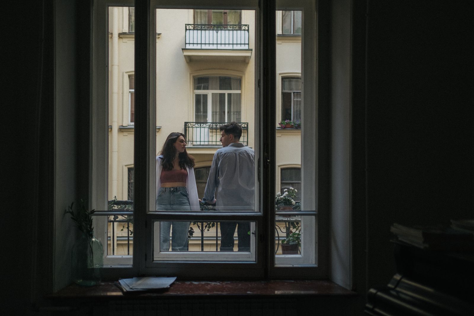 Couple enjoying a moment together on a balcony, framed by a window.