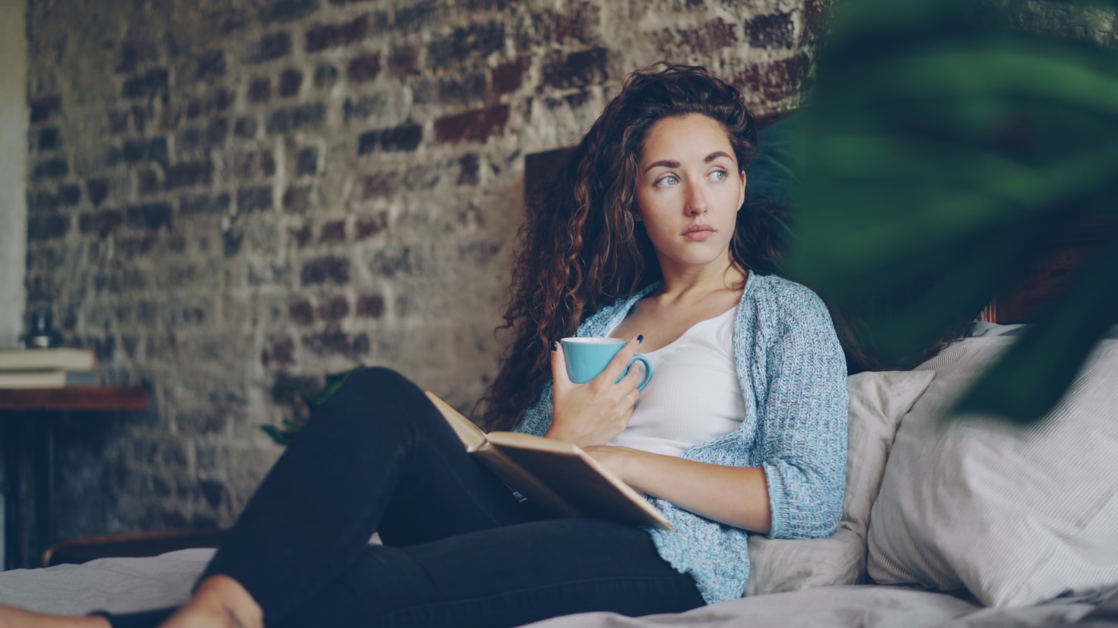 Woman holding coffee cup reading book on bed
