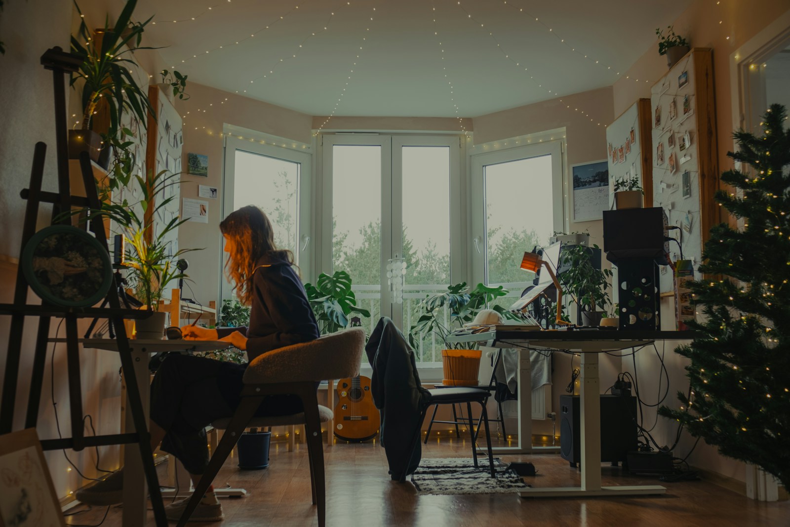 Woman working at a desk in a cozy, plant-filled room.