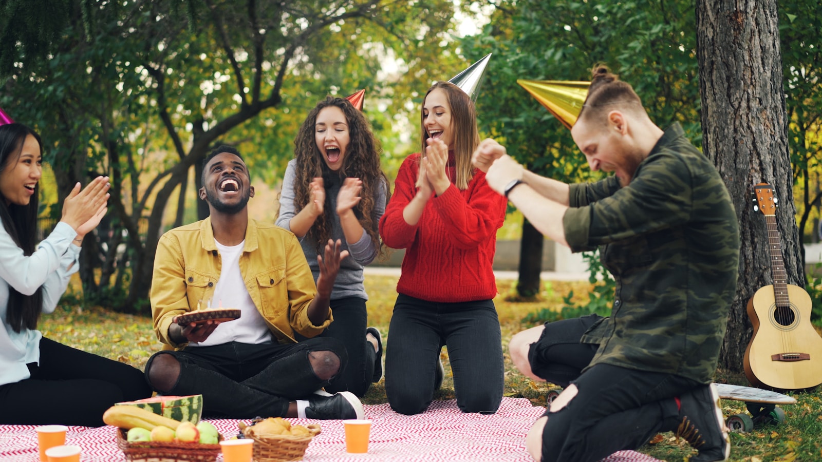 Friends celebrating a birthday outdoors with a cake.