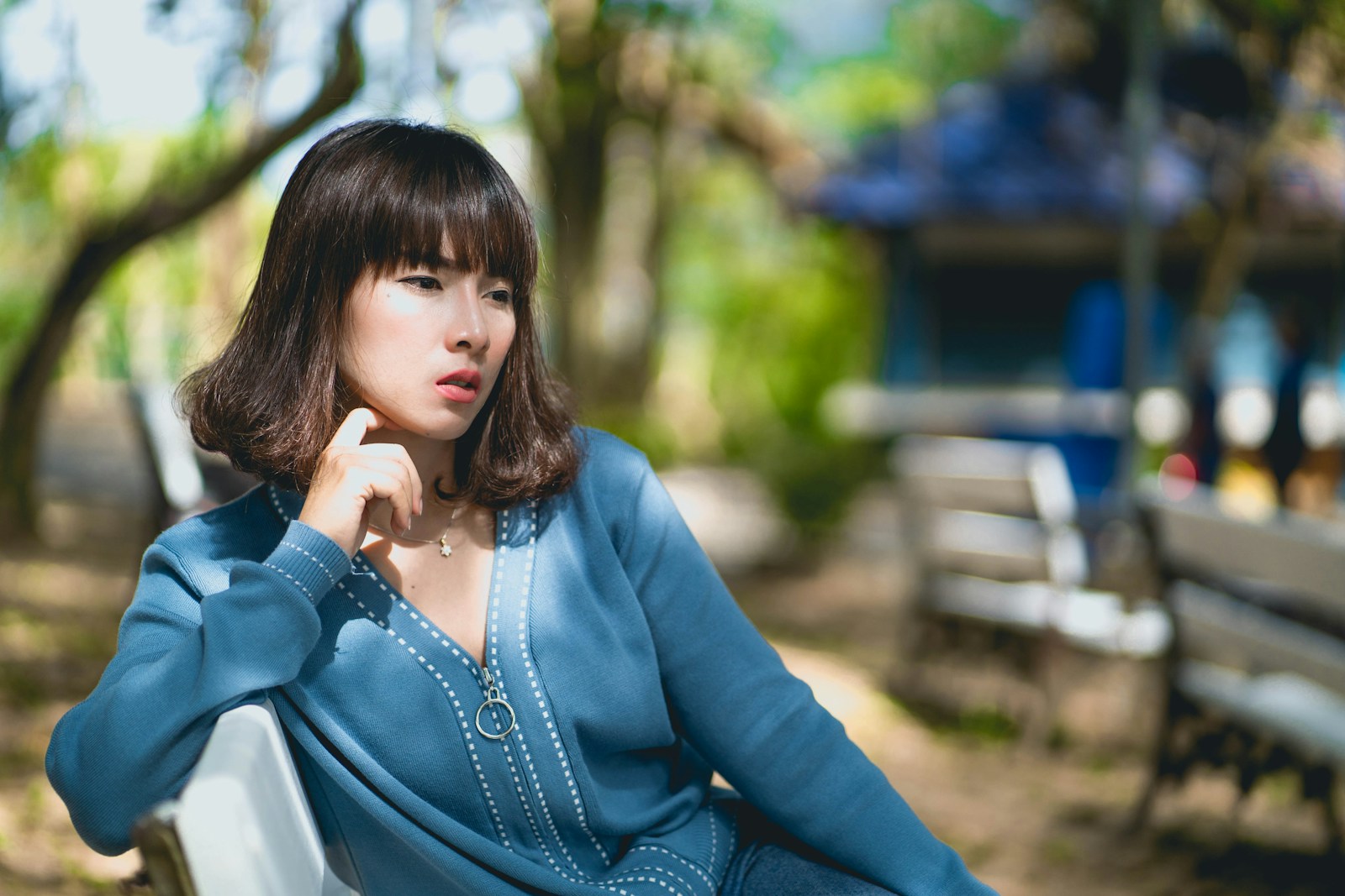 woman wearing blue long-sleeved blouse sitting on white bench