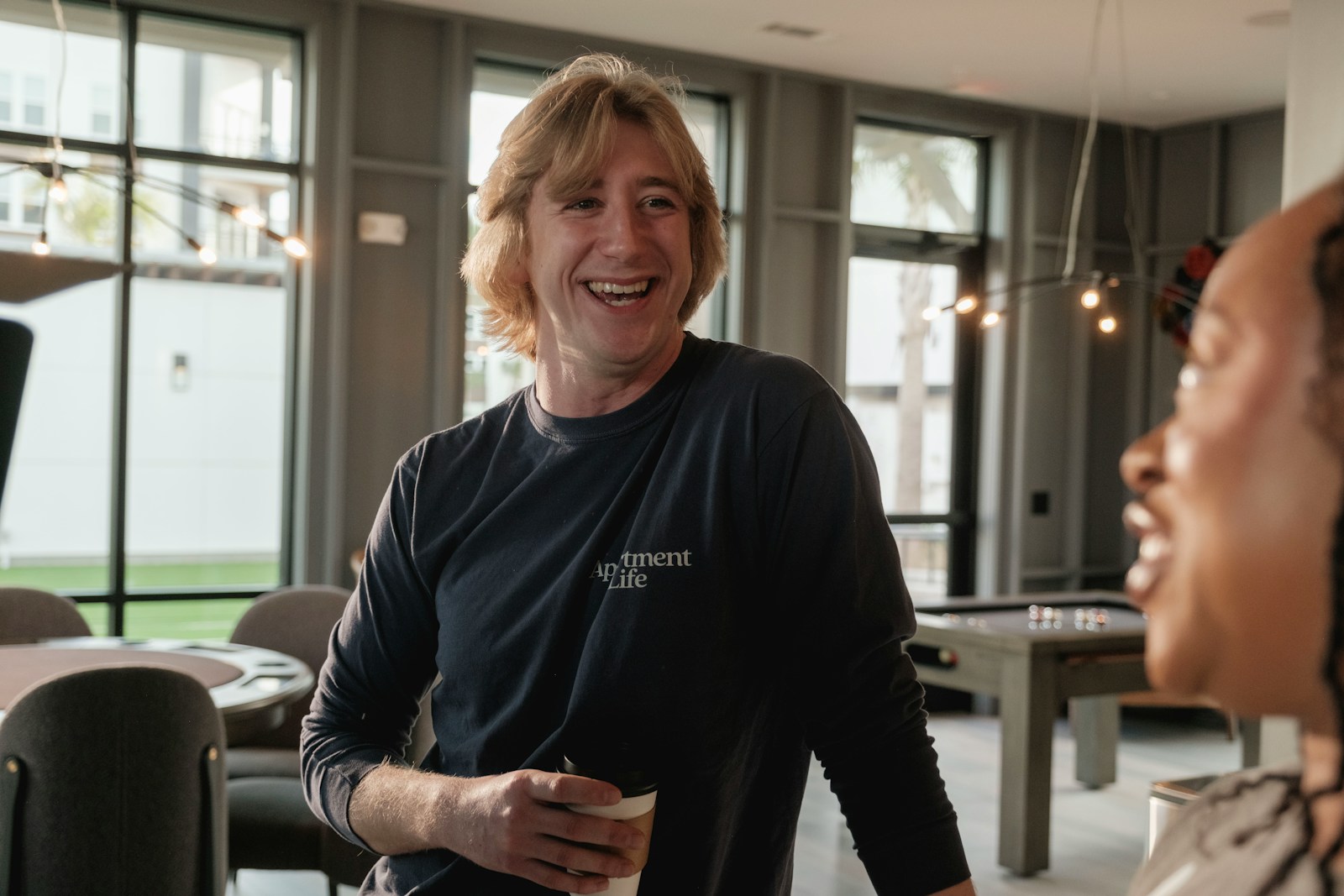 Man with blonde hair laughing while holding a drink