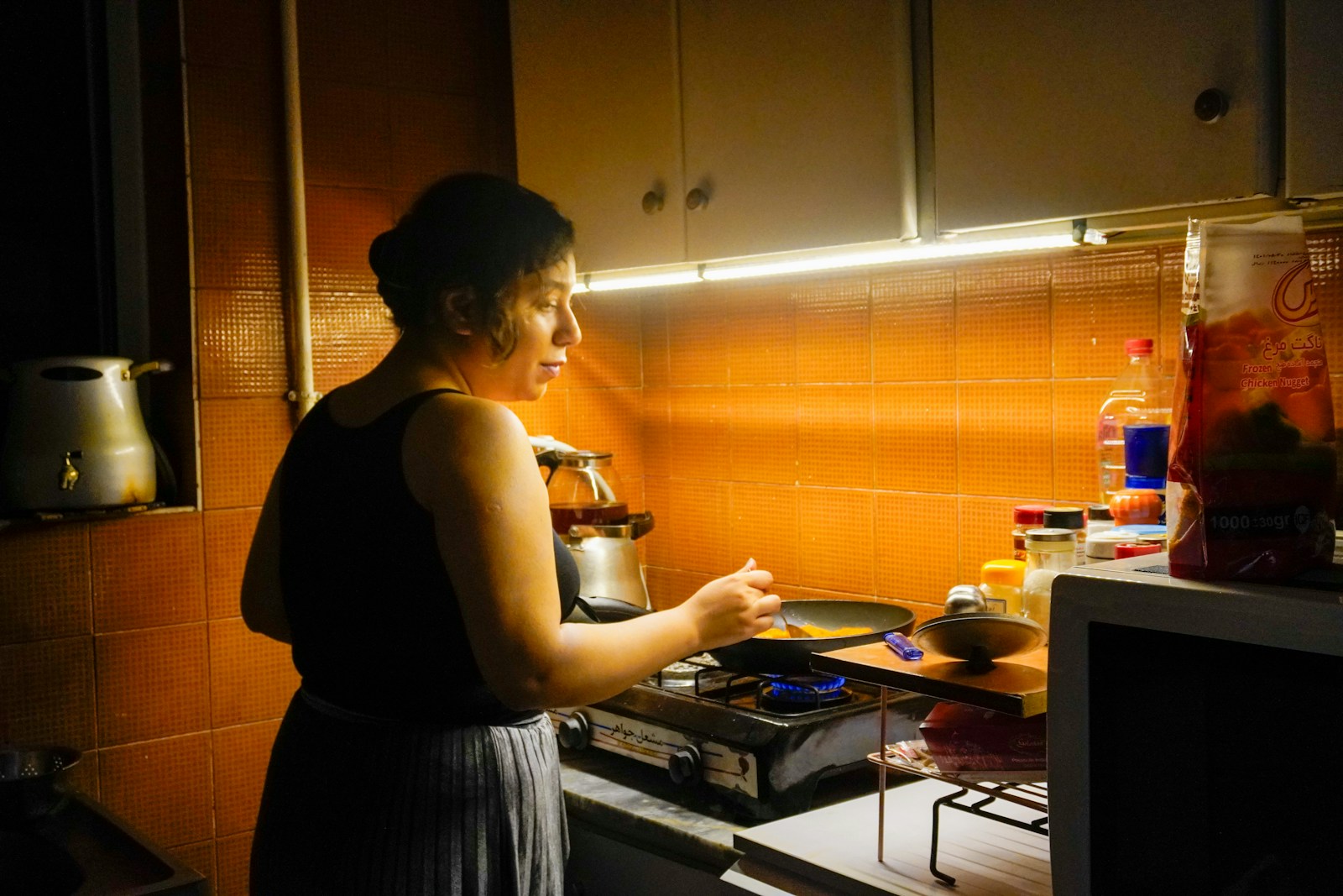 A woman cooks food in a small kitchen.