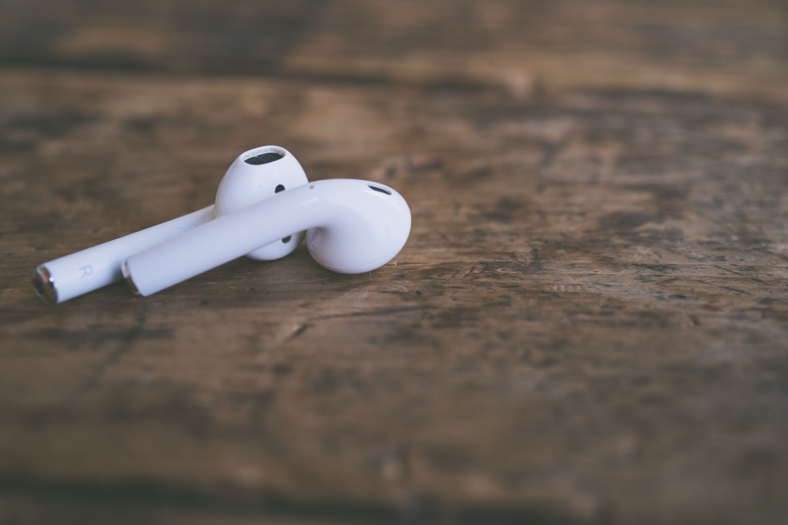 A pair of white wireless earbuds placed on rustic wooden surface, showcasing minimalist product design.