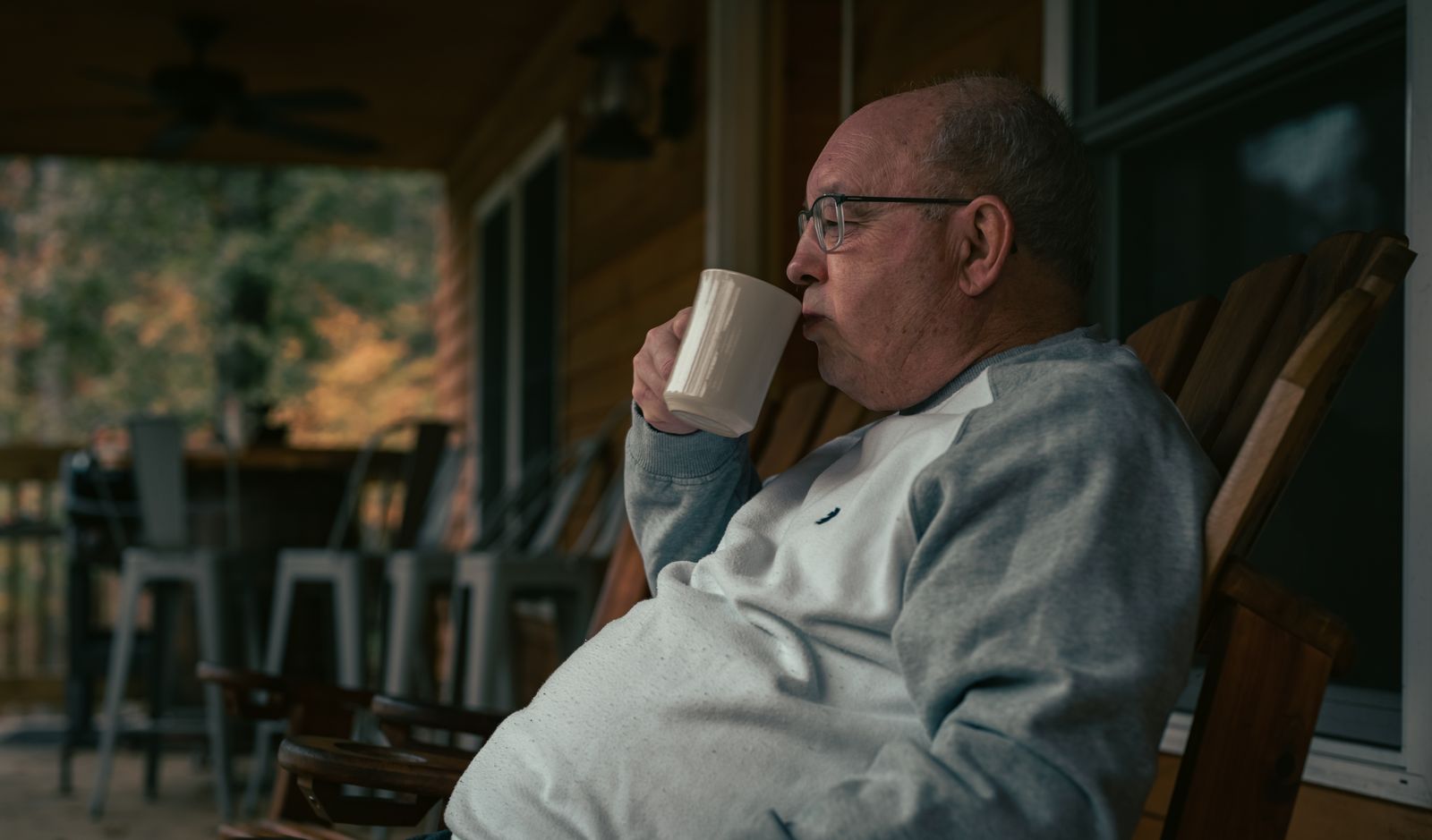 A senior man enjoying a warm beverage on a peaceful wooden porch in autumn.