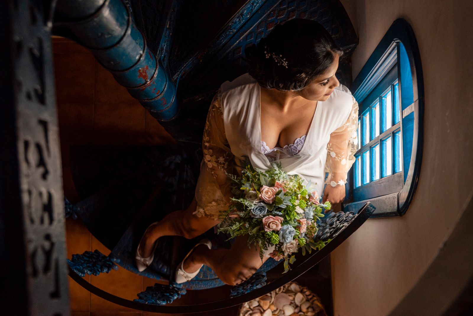 Aerial view of a bride in a robe holding a bouquet on a spiral staircase.