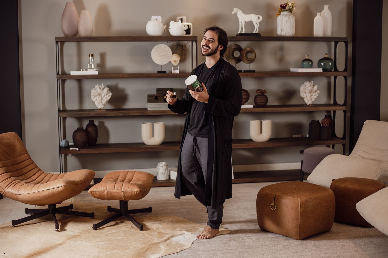 Man enjoying coffee in a modern living room with chic furniture and shelves.