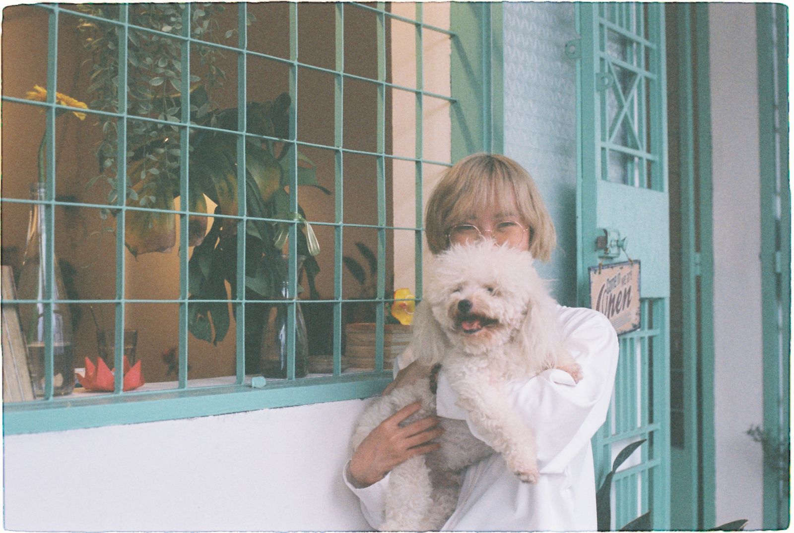 Woman lovingly holding a fluffy white dog in front of a charming home facade.