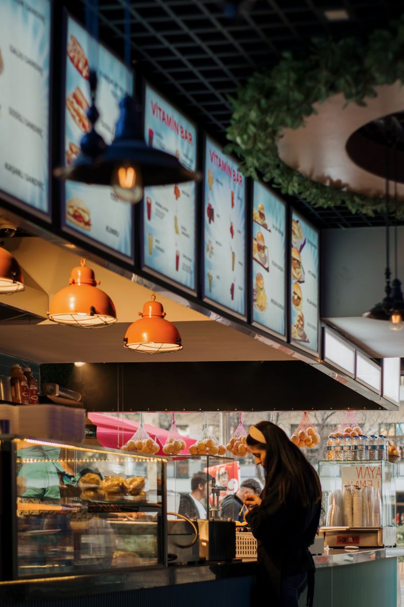 Contemporary bistro interior with illuminated menus and counter service, featuring a woman working.