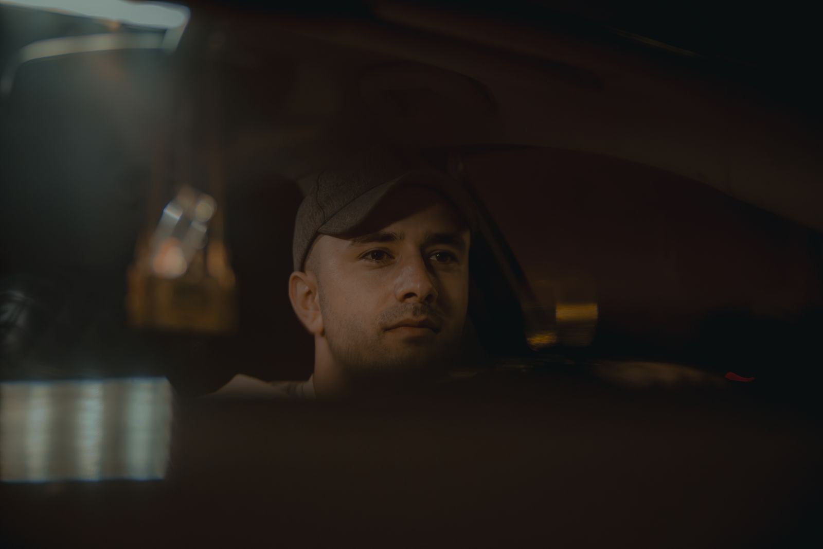 Young man driving at night, captured in a dim car interior with a cap on. Calm and focused expression.