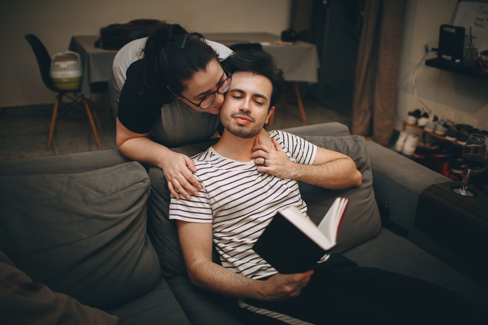 A couple enjoying a cozy moment indoors, reading on a sofa and embracing.