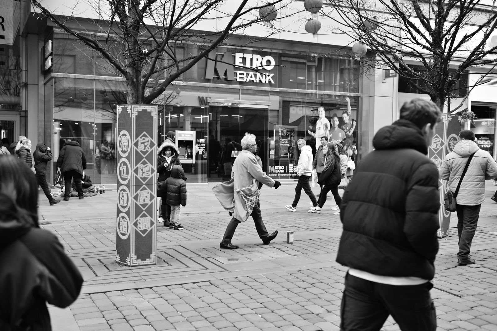Monochrome street view of people walking past a bank with decorative columns.
