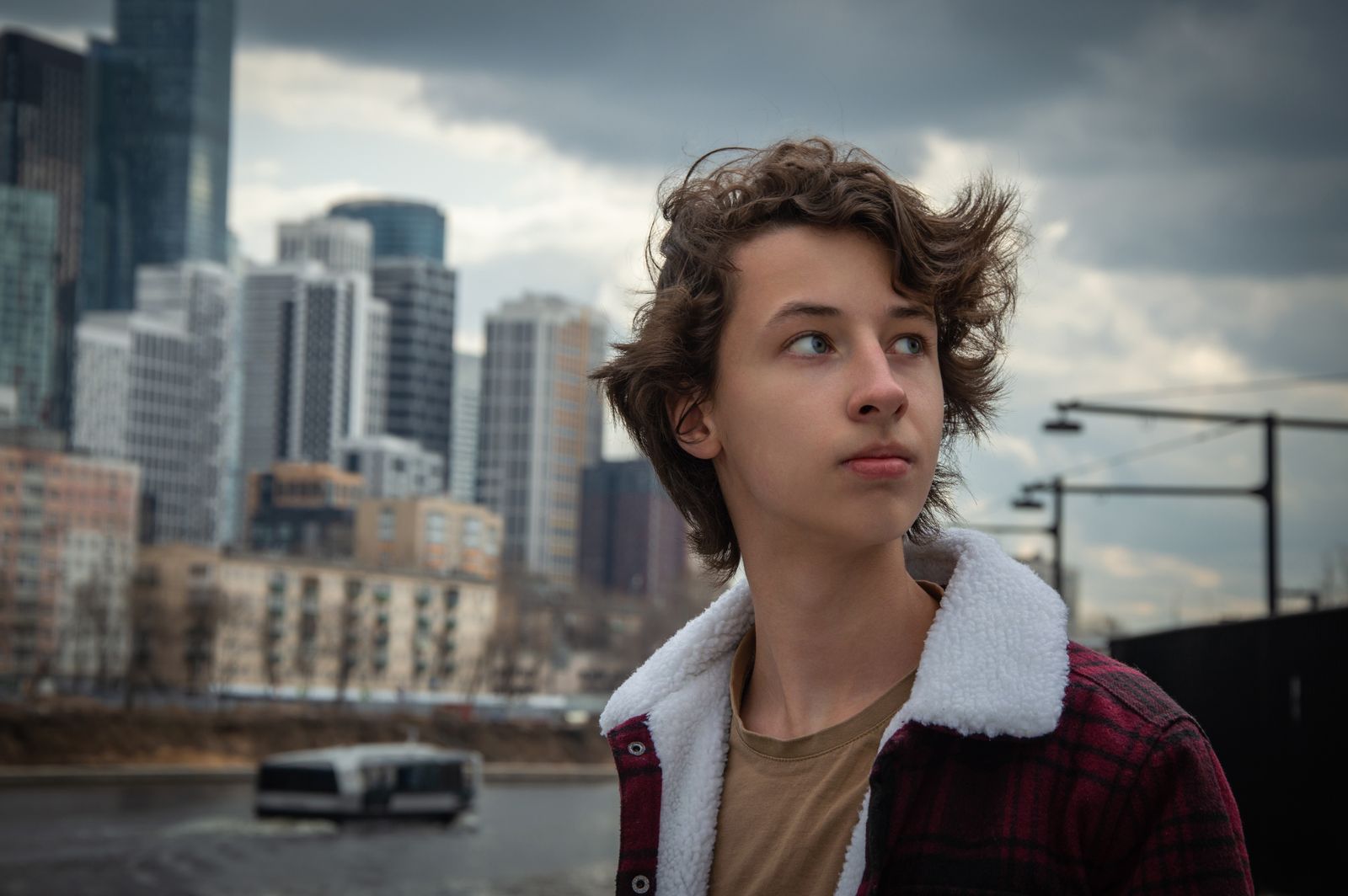 Teenager with stylish hair in an urban environment, featuring a modern city skyline in the background.