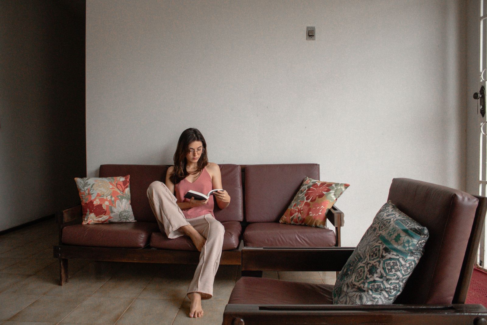 A woman reading a book on a minimalist couch, creating a peaceful indoor ambiance with floral cushions.