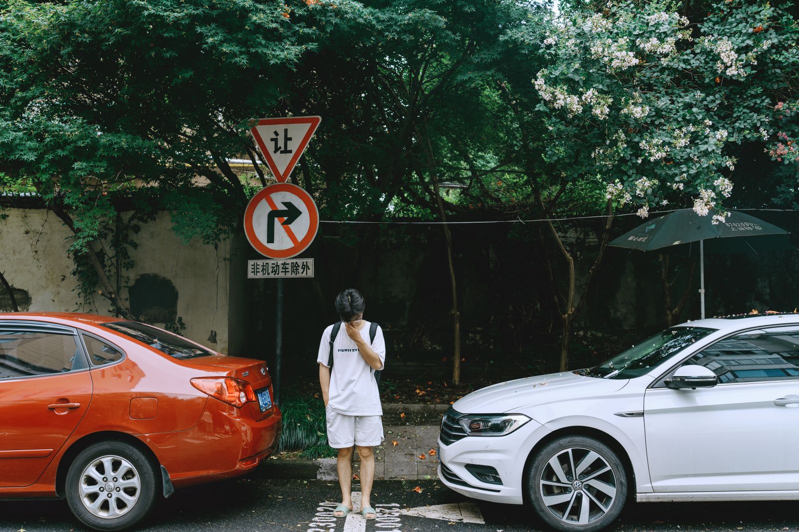 Man standing between parked cars in a green urban environment with signage.