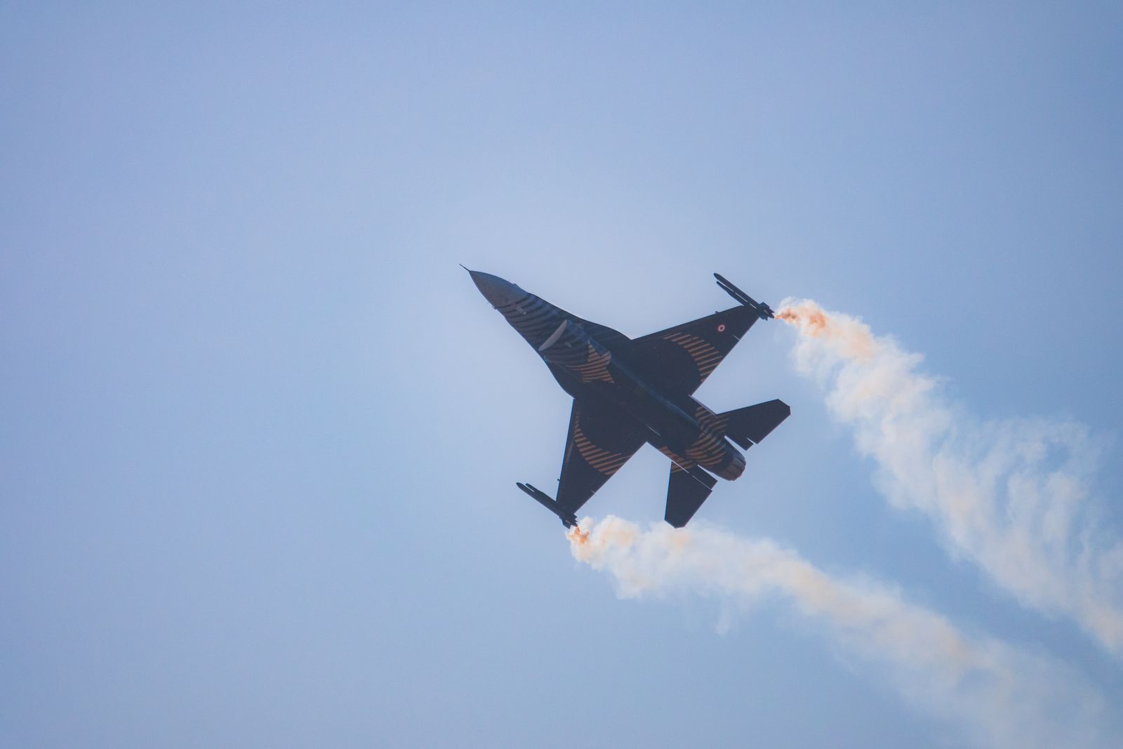 A military jet plane gracefully performs an aerial maneuver with smoke trails against a clear blue sky.