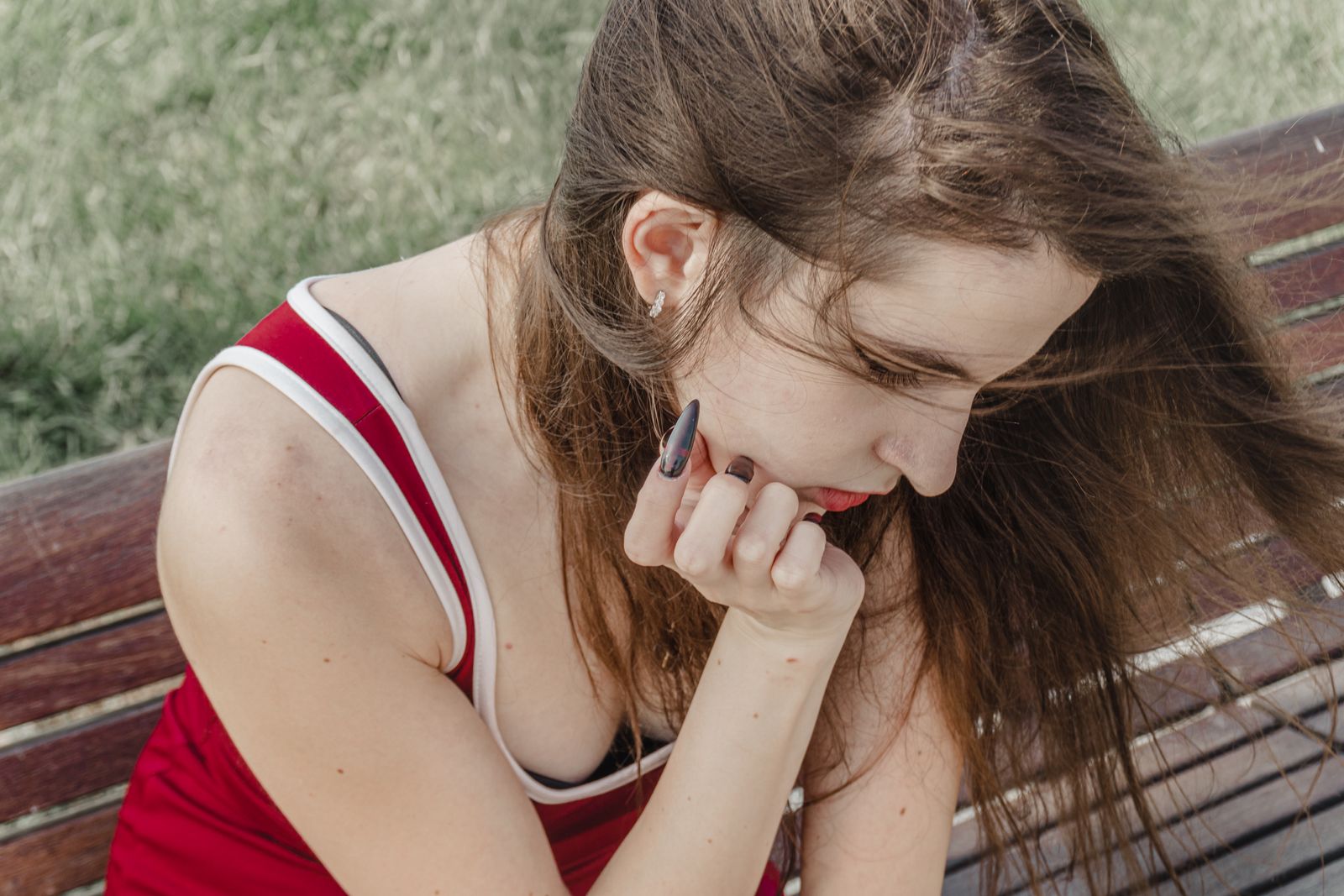 Young woman in a red tank top sitting on a wooden bench, deep in thought.