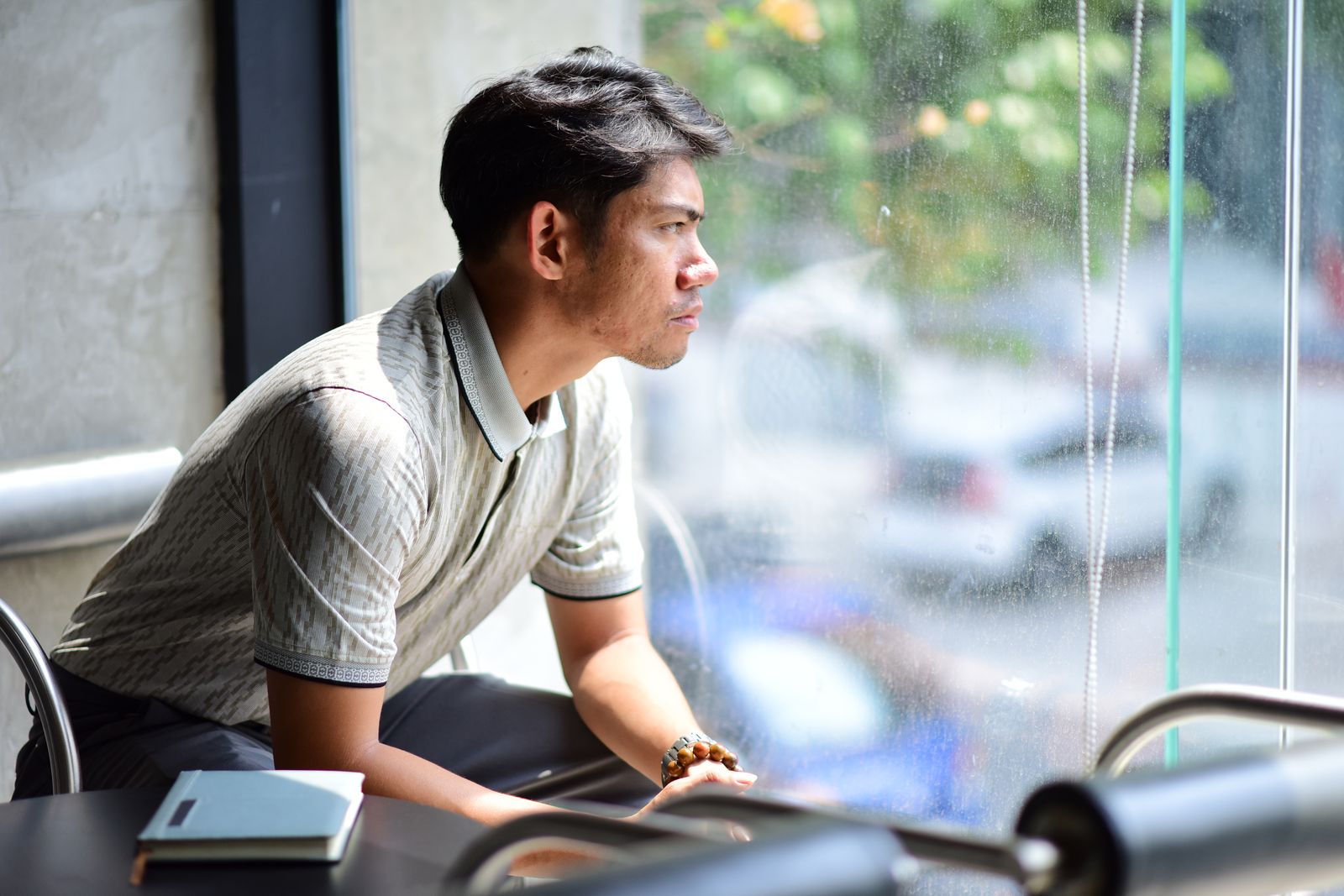 Man sitting by a window in a café, gazing outside in contemplation under soft daylight.